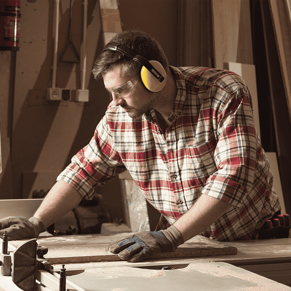 Tischler bei Arbeit mit Holzwerkstoffen trägt Kapselgehörschutz gegen Lärm am Arbeitsplatz.