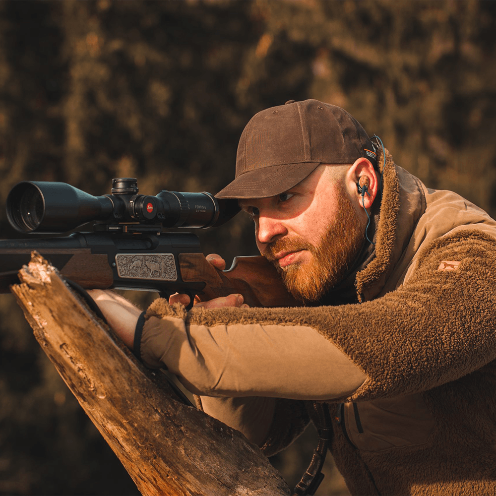Jäger mit Zielfernrohrgewehr trägt In-Ear-Gehörschutz zur Prävention von Knalltraumata.